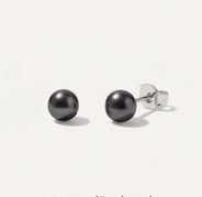 A pair of 5mm dainty round pearl stud earrings with silver posts, shown on a light cream background 