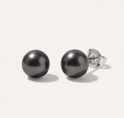 A pair of 7mm round black pearl stud earrings with silver posts, shown on a light beige background