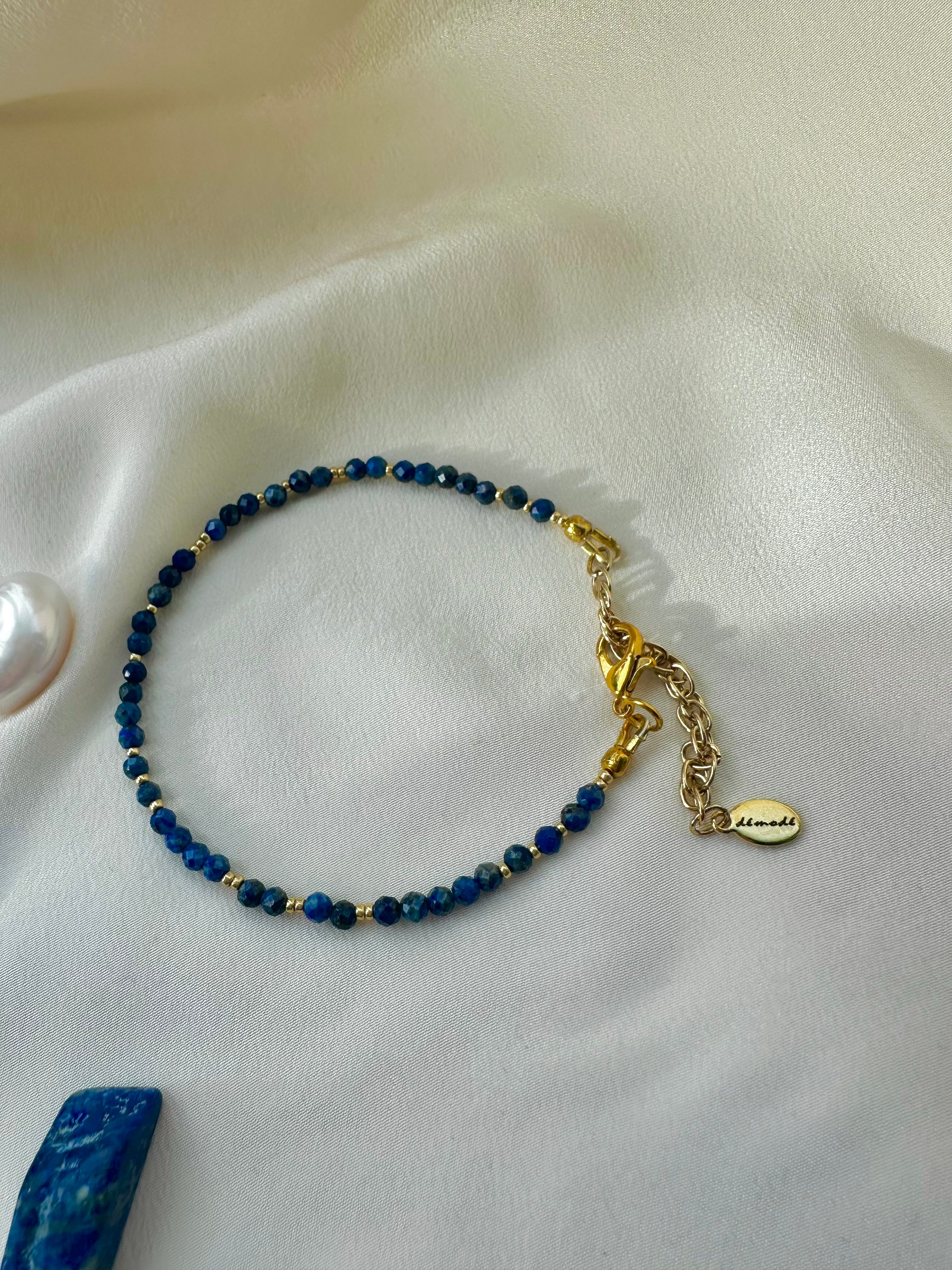 Blue beaded bracelet with gold chain on a white fabric background