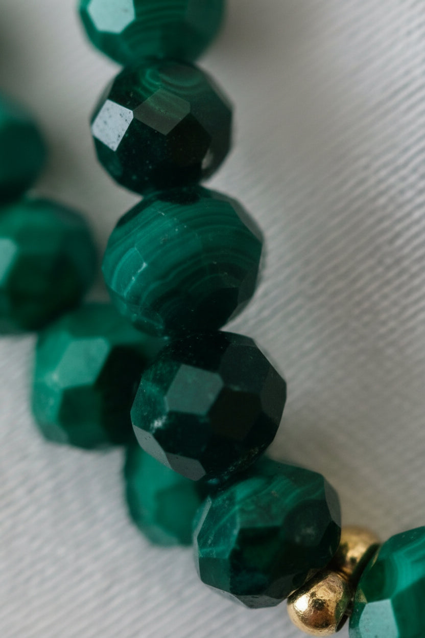 Close-up of green beads on a string with gold clasp against a textured beige background