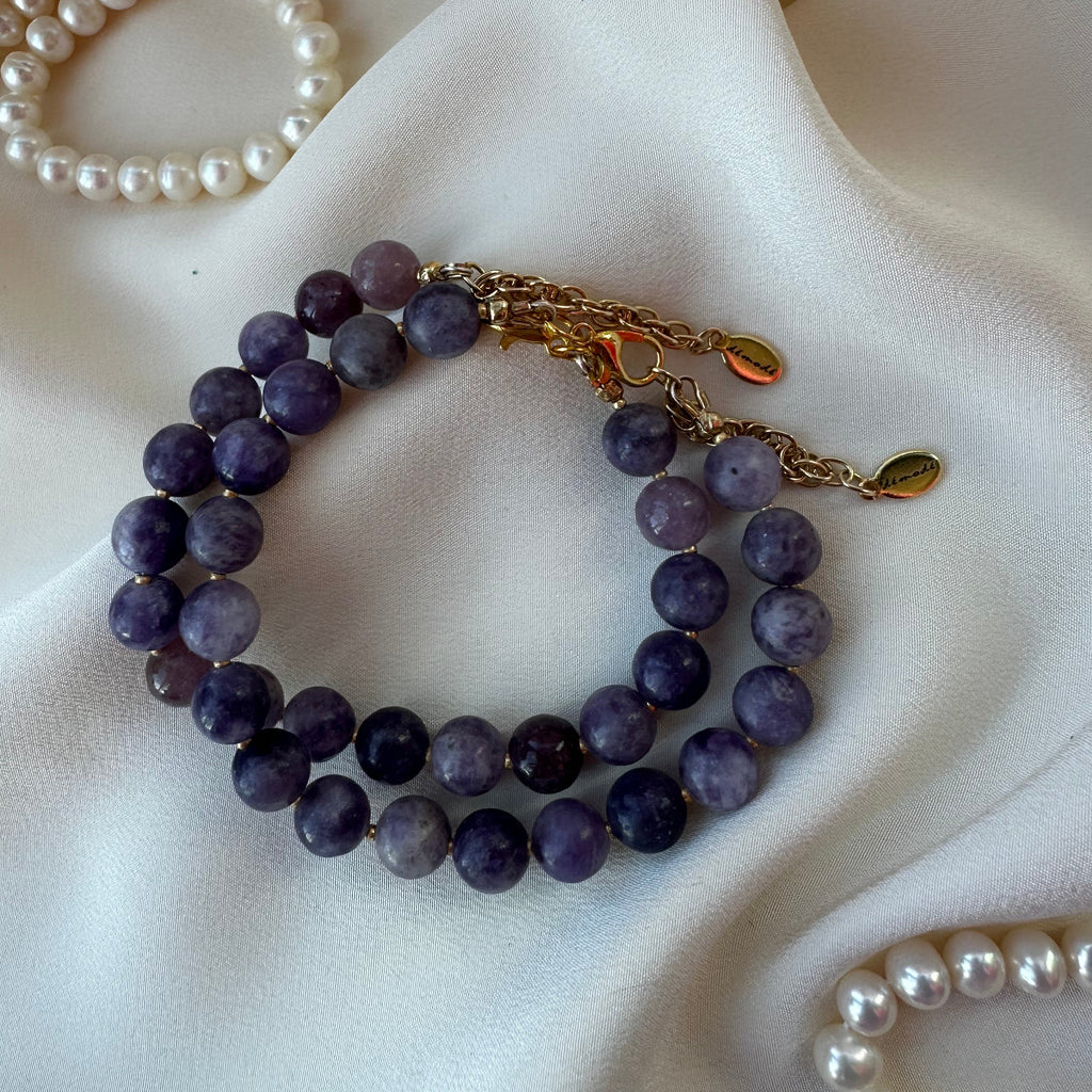 Purple Lepidolite beaded bracelet with gold clasp on a white fabric background