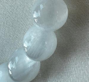 Bracelet with clear beads and a silver tag on a light gray background