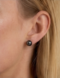 A close-up of a model's ear wearing a single round black pearl stud earring.
