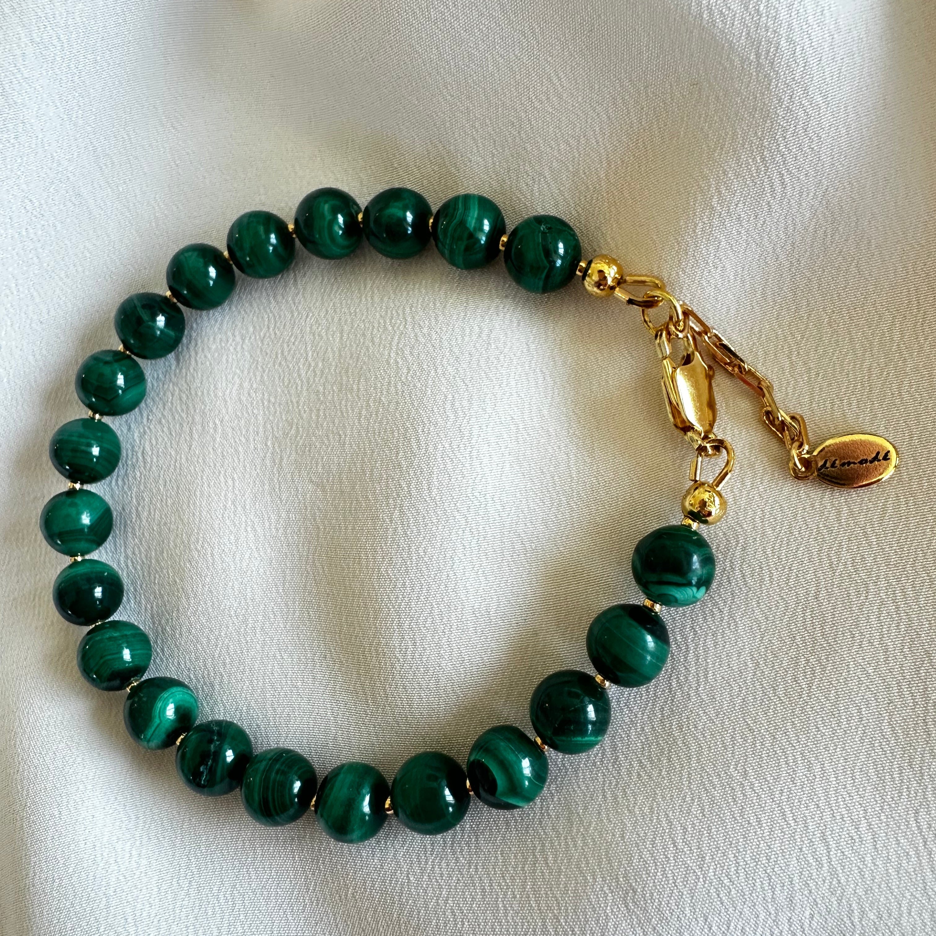 Green beaded bracelet with gold clasp on a white fabric background