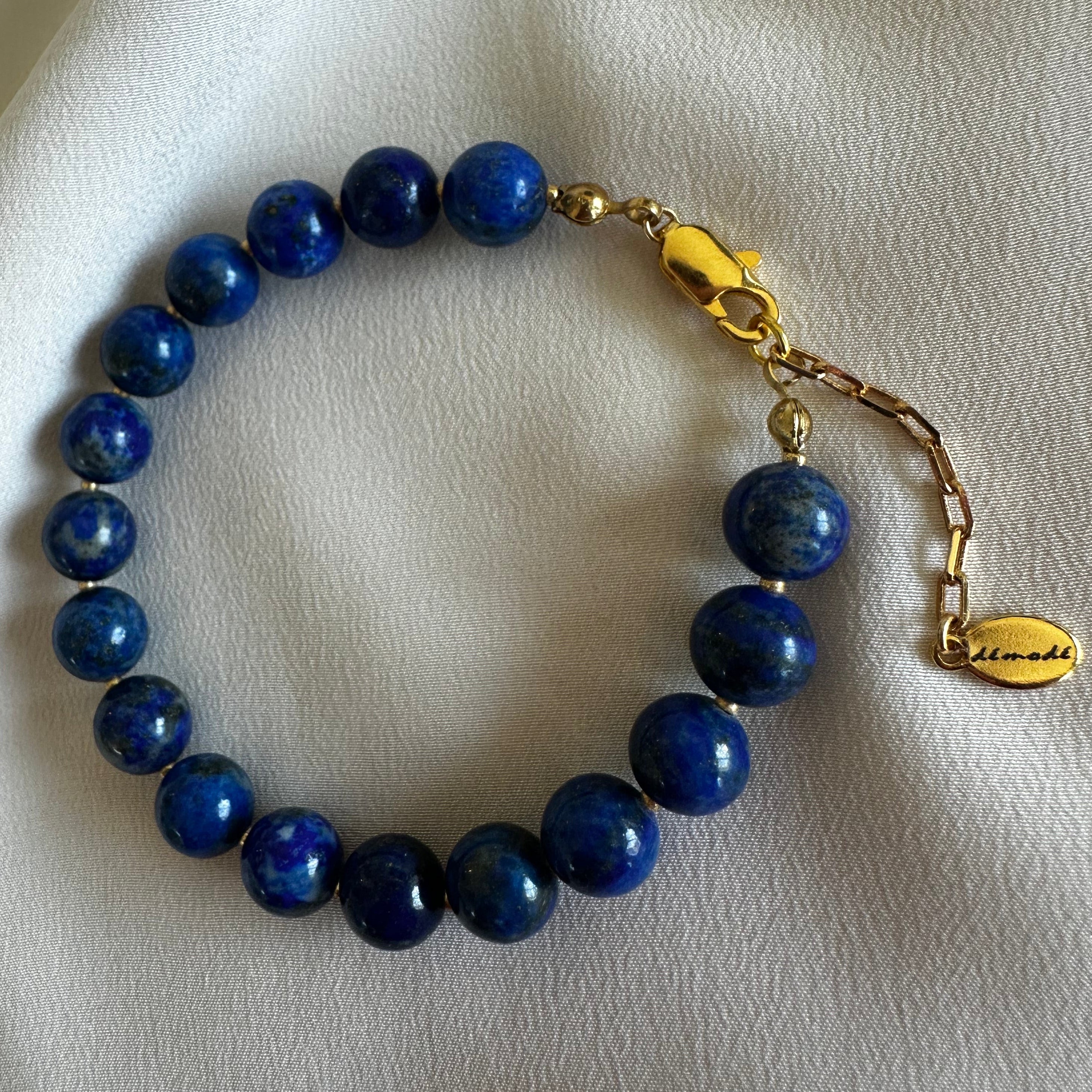 Lapis Lazuli Blue beaded bracelet with gold clasp on a white fabric background