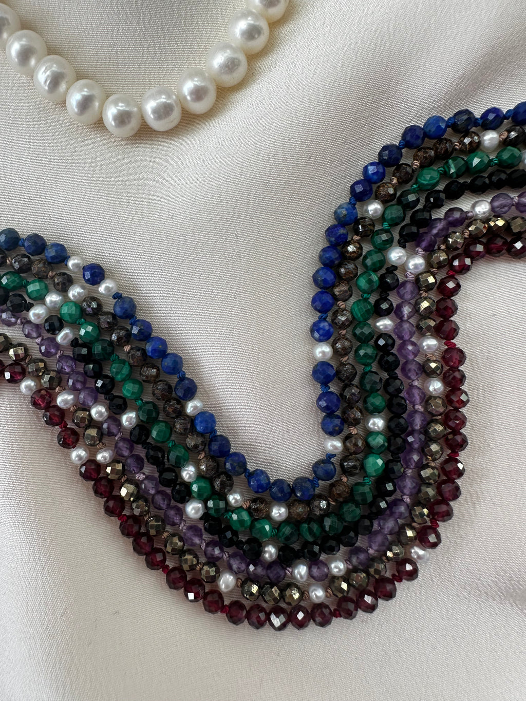 Colorful beaded necklace and white pearl necklace on a light background