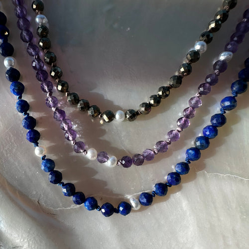 Three beaded necklaces in blue, purple, and white on a textured surface